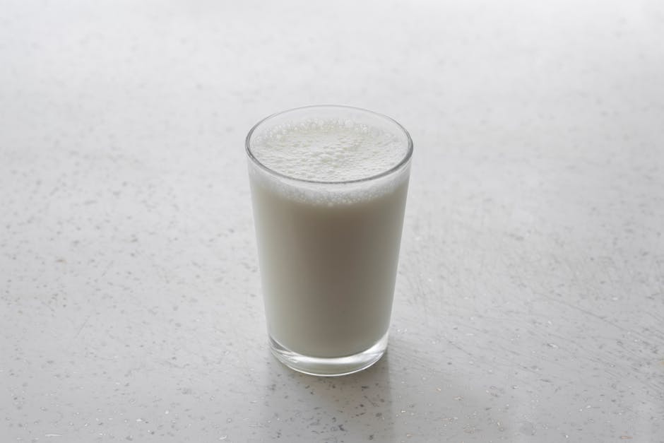 A frothy glass of milk on a textured white surface, captured with minimalism.